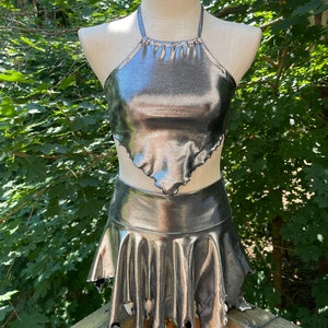 May include: A silver metallic halter top and skirt set with a ruffled hem. The skirt has a jagged, frayed edge.