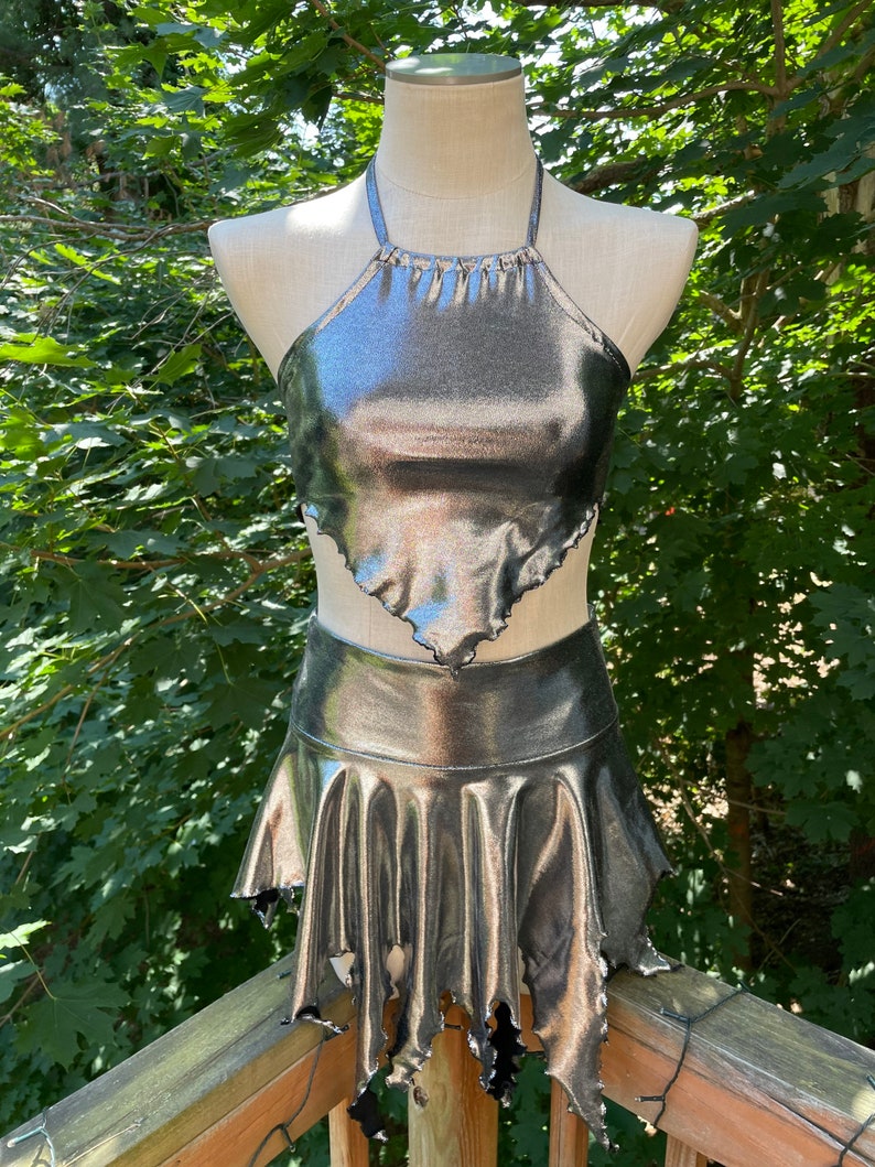 May include: A silver metallic halter top and skirt set with a ruffled hem. The skirt has a jagged, frayed edge.