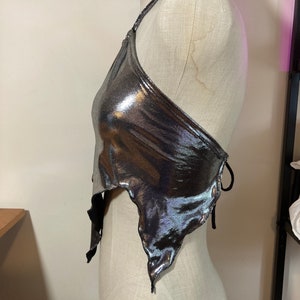 May include: A silver metallic halter top with a tie closure at the back. The top has a draped, asymmetrical design and a slightly cropped length.