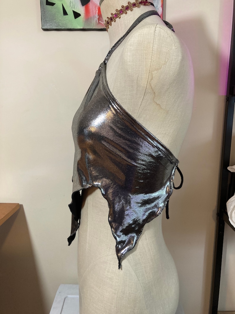 May include: A silver metallic halter top with a tie closure at the back. The top has a draped, asymmetrical design and a slightly cropped length.