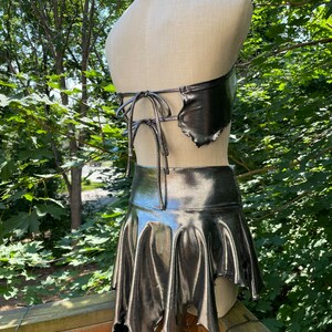 May include: A silver metallic halter top and skirt set with a jagged, asymmetrical hemline. The top has a tie closure at the back.