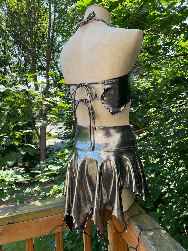 May include: A silver metallic halter top and skirt set with a jagged, asymmetrical hemline. The top has a tie closure at the back.