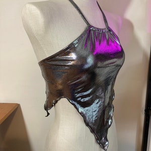 May include: A silver metallic halter top with a purple iridescent sheen. The top has a ruffled neckline and a loose, flowing fit.