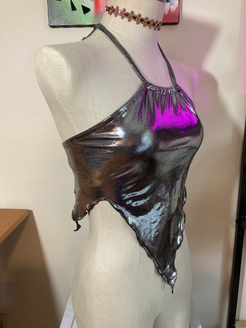 May include: A silver metallic halter top with a purple iridescent sheen. The top has a ruffled neckline and a loose, flowing fit.
