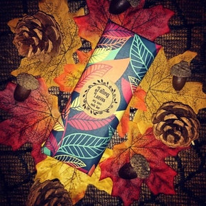 May include: A soy wax melt bar wrapped in paper with a fall leaf design. The paper has a round sticker that says "Falling Leaves soy wax melt bar". The bar is surrounded by fall leaves.