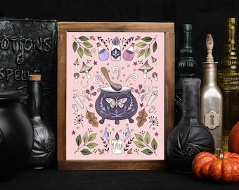 May include: A pink and brown framed print with a whimsical illustration of a cauldron, potion bottles, crystals, and a butterfly. The text "Potions & Spells" is visible on a black book in the background.