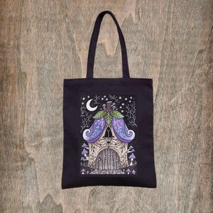 Peut inclure: Sac fourre-tout noir avec une illustration fantaisiste d'une maison faite de feuilles et de branches, entourée de champignons et d'étoiles. La maison a une porte en bois et une lune croissante dans le ciel.