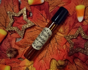 May include: A small brown glass bottle with a black rollerball top and a white label that reads "Rotten Pumpkin" original perfumed oil. The bottle is surrounded by autumnal decorations, including orange and yellow leaves, candy corn, and gold stars.