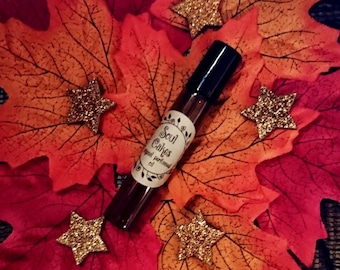 May include: A brown glass roll-on bottle with a black cap and a white label that says "Soul Cakes - Special Perfume Oil". The bottle is surrounded by red and orange autumn leaves and gold glitter stars.