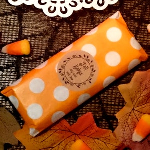 May include: A small orange and white polka dot gift bag with a brown label that says "Fall Bakes" with a small twig design. The bag is surrounded by fall leaves and candy corn.