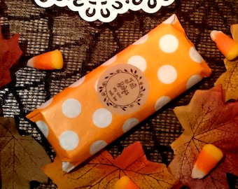May include: A small orange and white polka dot gift bag with a brown label that says "Fall Bakes" with a small twig design. The bag is surrounded by fall leaves and candy corn.