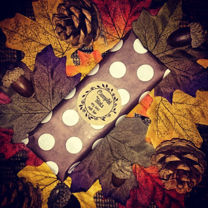 May include: A brown and white polka dot gift wrap with a round label that says "Campfire Treats" soy wax melt bar. The gift wrap is surrounded by fall leaves and pine cones.