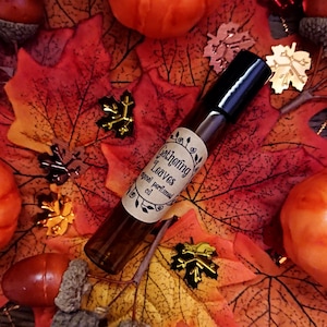 May include: A brown glass roll-on bottle with a black cap. The bottle has a label that says "Gathering of Leaves Original Perfumed Oil". The bottle is surrounded by autumn-coloured leaves and pumpkins.