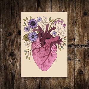 May include: A pink anatomical heart with a detailed illustration of the chambers and veins, surrounded by a bouquet of purple and white flowers. The flowers include delicate blossoms and leaves, creating a whimsical and romantic design.