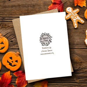 Puede incluir: Una tarjeta de felicitaci&oacute;n con tem&aacute;tica de Halloween con un sobre de papel kraft, rodeada de galletas de Halloween y hojas de oto&ntilde;o. Las galletas incluyen una calabaza, un fantasma y un esqueleto. La tarjeta tiene un logotipo circular y texto.