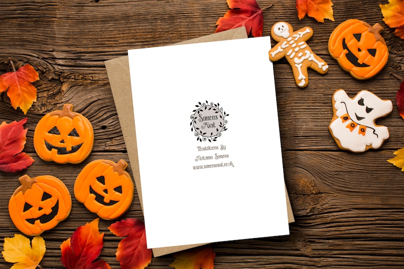 Puede incluir: Una tarjeta de felicitaci&oacute;n con tem&aacute;tica de Halloween con un sobre de papel kraft, rodeada de galletas de Halloween y hojas de oto&ntilde;o. Las galletas incluyen una calabaza, un fantasma y un esqueleto. La tarjeta tiene un logotipo circular y texto.