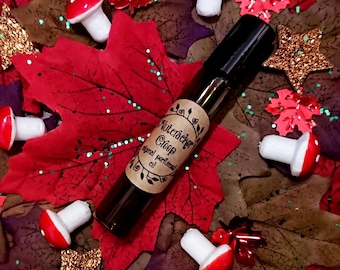 May include: A brown glass bottle with a brown paper label that reads "Nutcracker Creep Original Perfumed Oil". The bottle is surrounded by red and green fall leaves and white mushrooms.