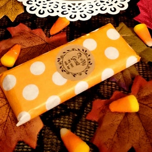 May include: A small orange and white polka dot gift bag with a brown paper label that says "Oh My Goods" and "Made with Love" on it. The bag is surrounded by fall leaves and candy corn.
