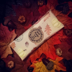 May include: A white tube with a brown label that says "Spiced Pumpkin Leaf" and is surrounded by fall leaves.