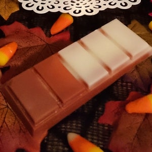 May include: A brown and white wax melt bar with five sections. The bar is surrounded by fall leaves and candy corn.