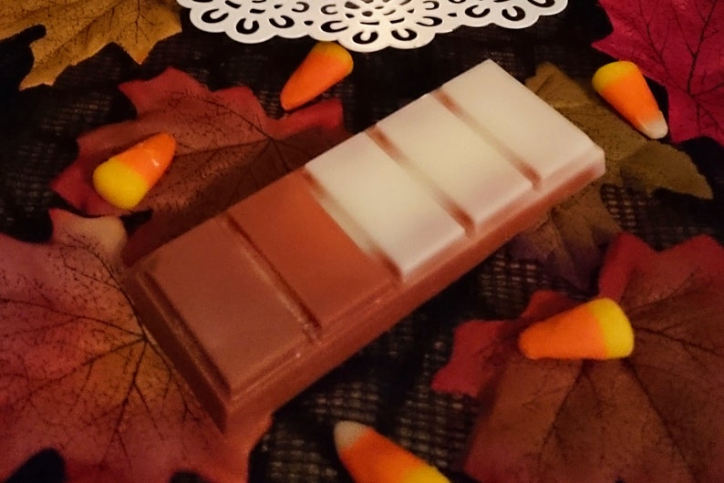May include: A brown and white wax melt bar with five sections. The bar is surrounded by fall leaves and candy corn.