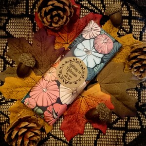 May include: A soy wax melt bar with a floral design featuring pumpkins and the text "Halfway to Halloween". The bar is wrapped in brown paper with a white circle label.