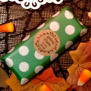 May include: A green and white polka dot wrapped bar of soap with a brown label that says "Delicious & Happy" with a leaf design. The soap is surrounded by fall leaves and candy corn.