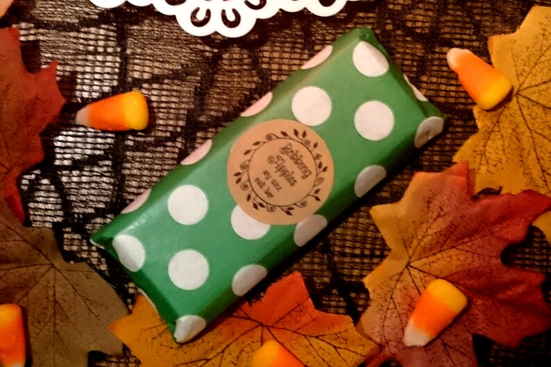 May include: A green and white polka dot wrapped bar of soap with a brown label that says "Delicious & Happy" with a leaf design. The soap is surrounded by fall leaves and candy corn.