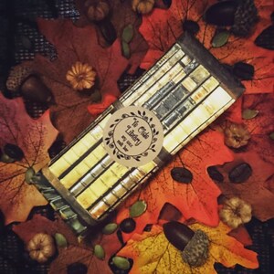 May include: A brown paper wrapped bar of soy wax with a label that reads "Ye Olde Library" with a decorative border. The bar is surrounded by fall leaves and acorns.