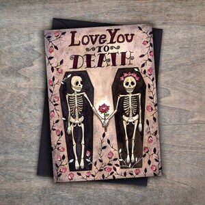Puede incluir: Una tarjeta de felicitaci&oacute;n con una ilustraci&oacute;n de acuarela de dos esqueletos tomados de la mano en ata&uacute;des rodeados de rosas rosas. El texto de la tarjeta dice "Love You To Death."