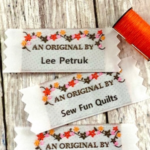 May include: Three white fabric labels with scalloped edges and floral embroidery. Each label reads "An Original By" followed by a name: Lee Petruk, Sew Fun Quilts, and Nana Andrea.