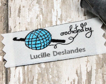 May include: White woven label with a black and blue crochet hook and yarn ball design. The text "Crocheted by Lucille Deslandes" is printed on the label.