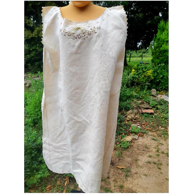 May include: A white sleeveless dress with delicate lace detailing around the neckline and a small bow at the center. The dress is made of a lightweight fabric and has a simple, elegant design.