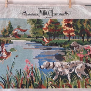 May include: Tapestry depicting a tranquil landscape with a lake, trees, and ducks in flight. Two dogs are shown near the water's edge. The tapestry has the text "MARGOT de Paris" at the top.