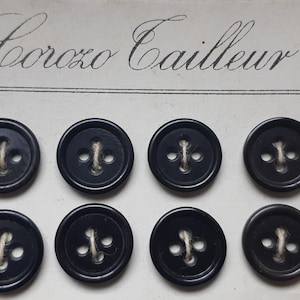 May include: A card with the text "Corozo Cailleur" printed on it. Eight black buttons with four holes and a white thread running through them are displayed on the card.