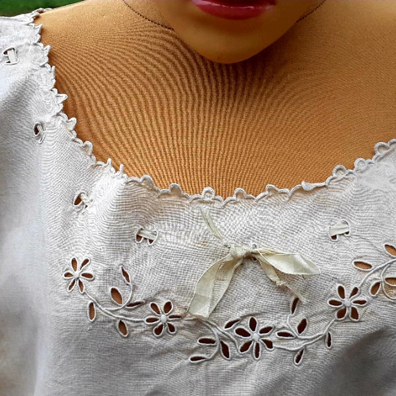 May include: White cotton top with a delicate lace trim and floral embroidery. The neckline features a small bow.