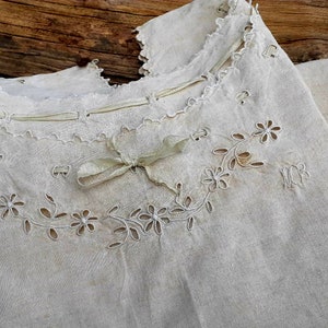 May include: A white linen garment with delicate floral embroidery and a ribbon tied at the neckline.