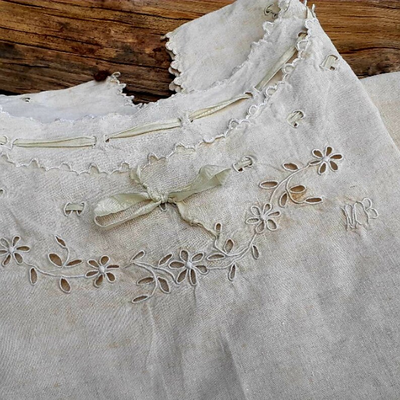May include: A white linen garment with delicate floral embroidery and a ribbon tied at the neckline.