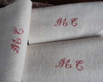 May include: Three white linen tea towels with red embroidered initials "M & C" on each towel.