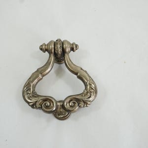 May include: A silver door knocker with an ornate design. The knocker is shaped like a ring with a decorative handle.