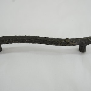 May include: A rustic, dark brown, metal cabinet pull shaped like a tree branch.