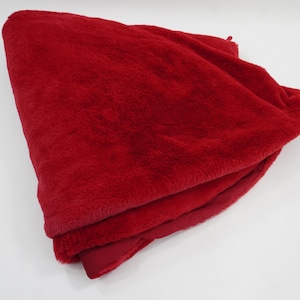 Puede incluir: Una manta doblada hecha de un material de piel sintética de color rojo vibrante. La tela tiene una textura densa, suave y afelpada con un color rojo intenso y uniforme. La manta está dispuesta en pliegues, mostrando el pelo grueso.