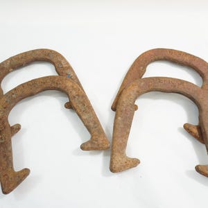 Könnte beinhalten: Zwei antike, rostige Metallhufeisen. Die Hufeisen haben eine verwitterte braune Farbe, mit einer gebogenen Oberseite und einem flachen Boden. Sie werden wahrscheinlich zu Dekorationszwecken verwendet.