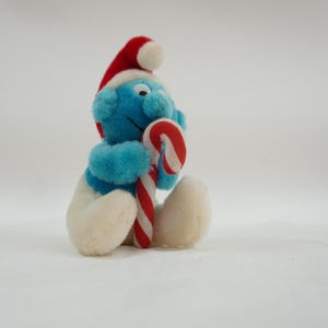 Op de afbeelding: Een blauw pluche speelgoedje met een rood-witte kerstmanmuts en een rood-witte snoepstok.