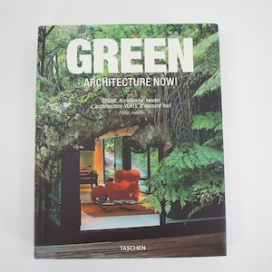 以下が含まれることがあります： 「GREEN ARCHITECTURE NOW!」という緑と白のタイトルが書かれた本の表紙。大きな窓と赤い椅子のある家の写真が載っている。家は緑豊かな植物に囲まれている。