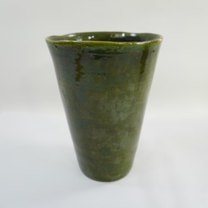 May include: A handcrafted, green ceramic vase with a slightly irregular rim. The vase has a tapered shape, wider at the top and narrowing towards the base. The surface has a mottled, glossy finish, showcasing variations in the green glaze.