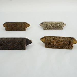 May include: Four ornate metal drawer pulls with intricate designs. The pulls are in different finishes: gold, silver, and two shades of bronze.