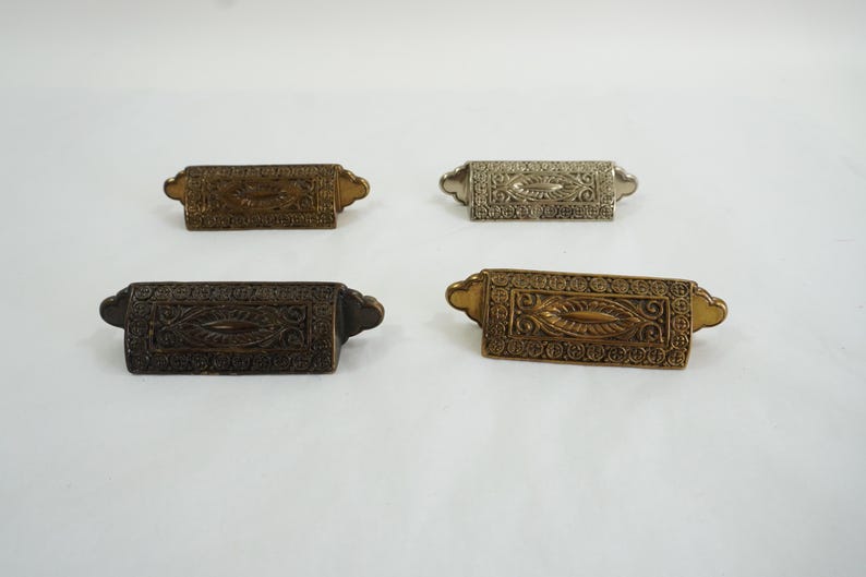May include: Four ornate metal drawer pulls with intricate designs. The pulls are in different finishes: gold, silver, and two shades of bronze.