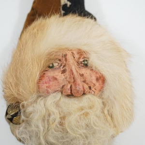 May include: A white fur-covered gnome head with a painted face, brown fur hat, and a long white beard.