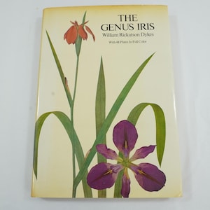 Può includere: Un libro con copertina rigida intitolato "The Genus Iris" di William Rickatson Dykes. La copertina presenta un'illustrazione ad acquerello di fiori di iris con petali viola e foglie verdi. Il libro ha uno sfondo color crema.